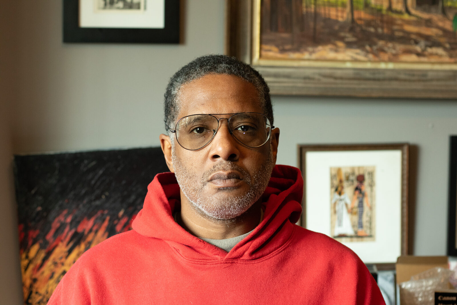 Portrait of Miguel Collins in a red hoodie in his art-filled home